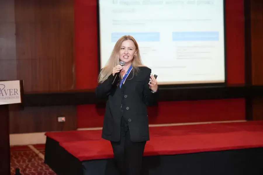 Kate V. on stage with a microphone, a slide headed “AI requires different security and privacy approach” behind her.
